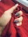 A hand with manicured nails holds a piece of red, textured fabric. The nails are painted in shades of dark purple and adorned with white decorative patterns and specks.