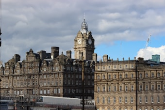 A historic building with an ornate facade and a prominent clock tower. The structure appears to be constructed from stone, exhibiting elaborate architectural details typical of a grand, old hotel or public building. The sky is partly cloudy, creating a classic and somewhat dramatic backdrop.