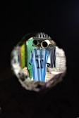 A blue and white striped jersey with the name 'Messi' and the number '10' is hanging on a line inside a room. The scene is viewed through a circular hole, giving a tunnel-like perspective. The background includes other garments and hints of patterned walls.