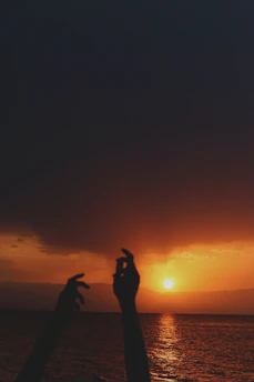 Hands raised in worship during an outdoor campus fellowship meeting at sunset.