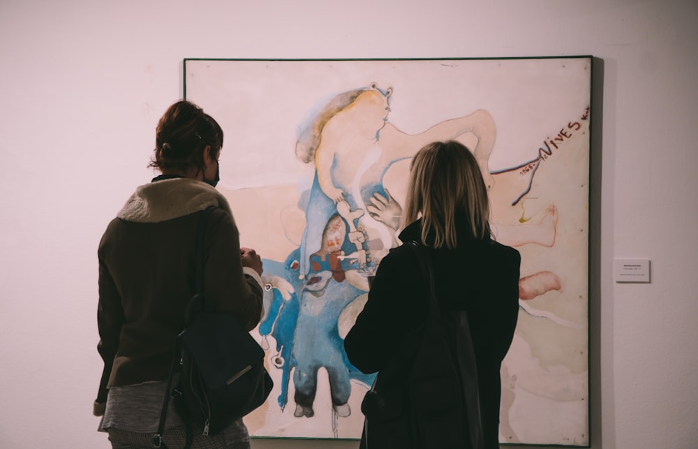 woman in black coat standing in front of wall with painting