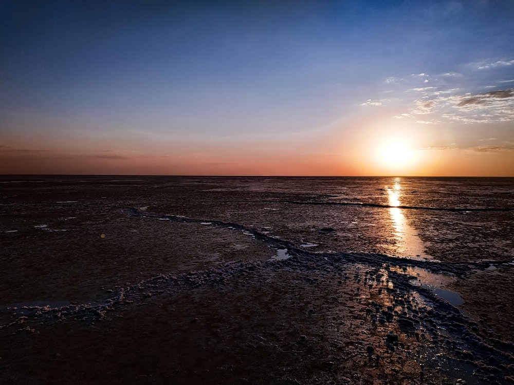 the sun is setting over the water on the beach