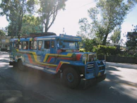 A colorful jeepney weaving through a lively Manila street filled with smiling locals.