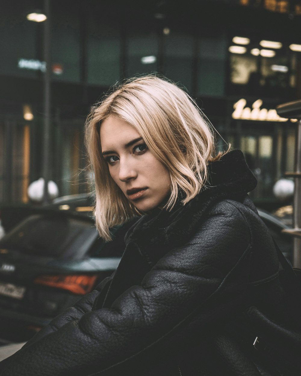 woman in black leather jacket standing near black car during night time