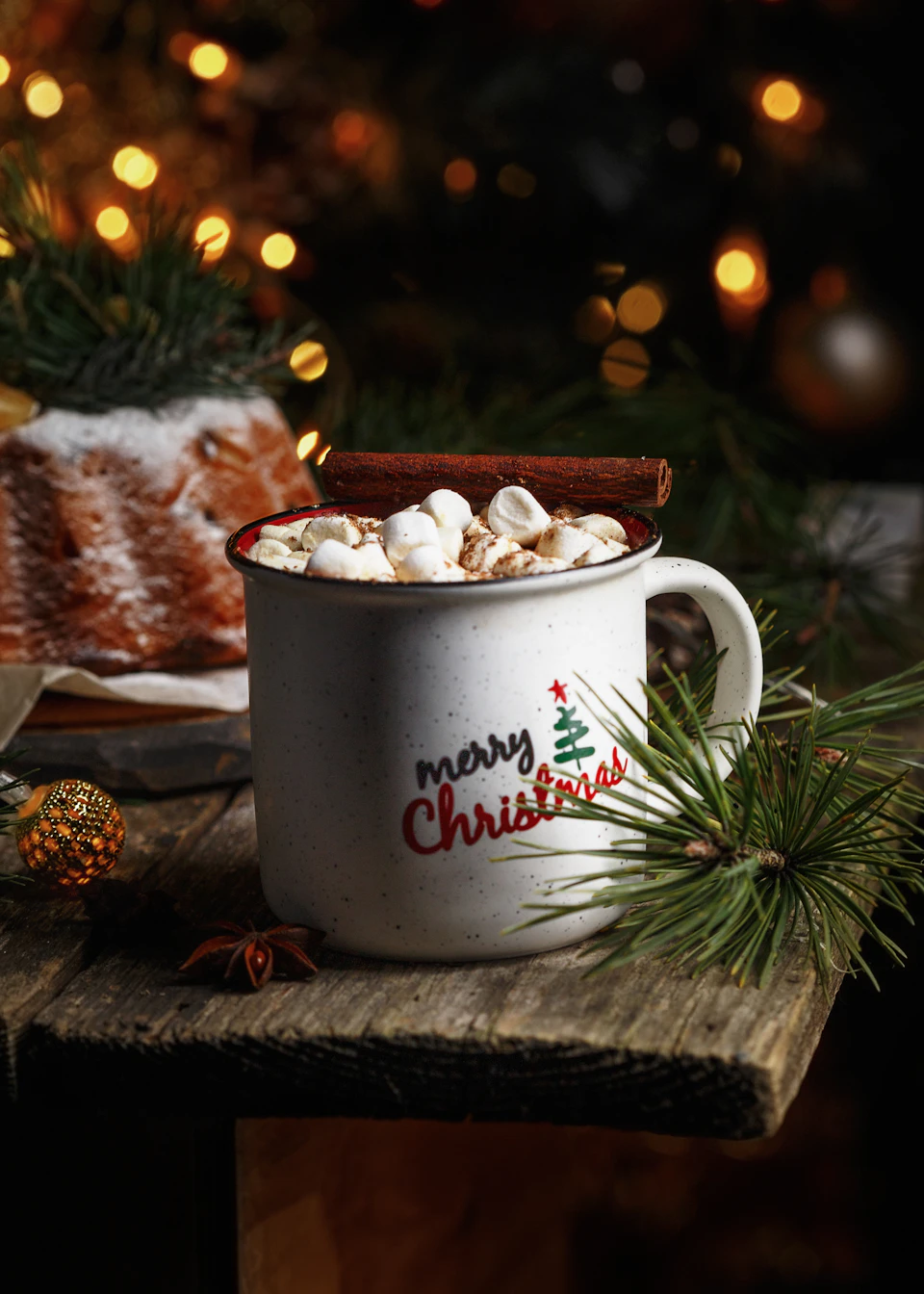 Christmas scene on wooden table with festive decorations including a white mug with red text