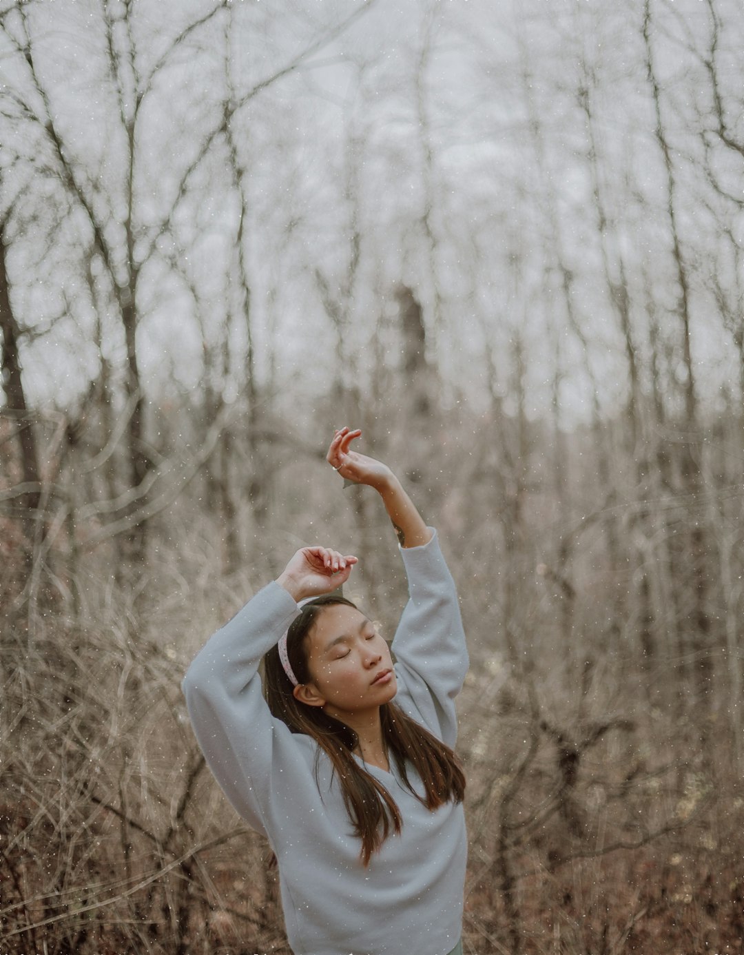 woman in white coat standing near bare trees during daytime