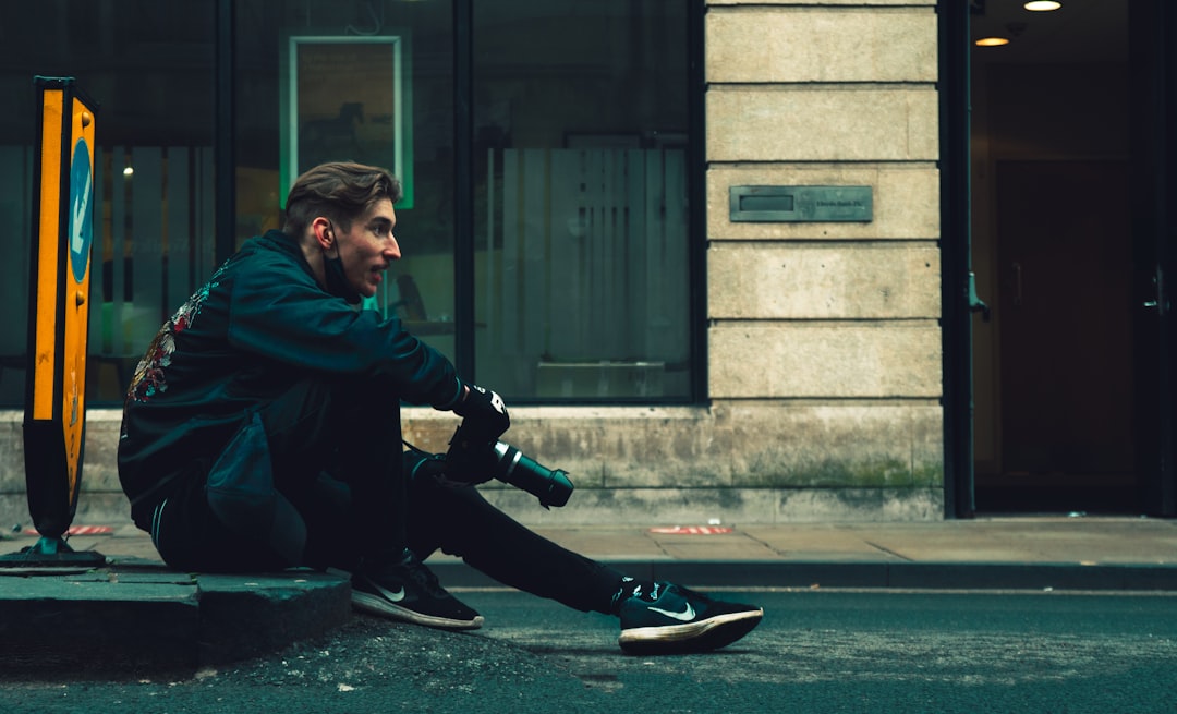 man in green hoodie and black pants sitting on sidewalk during daytime