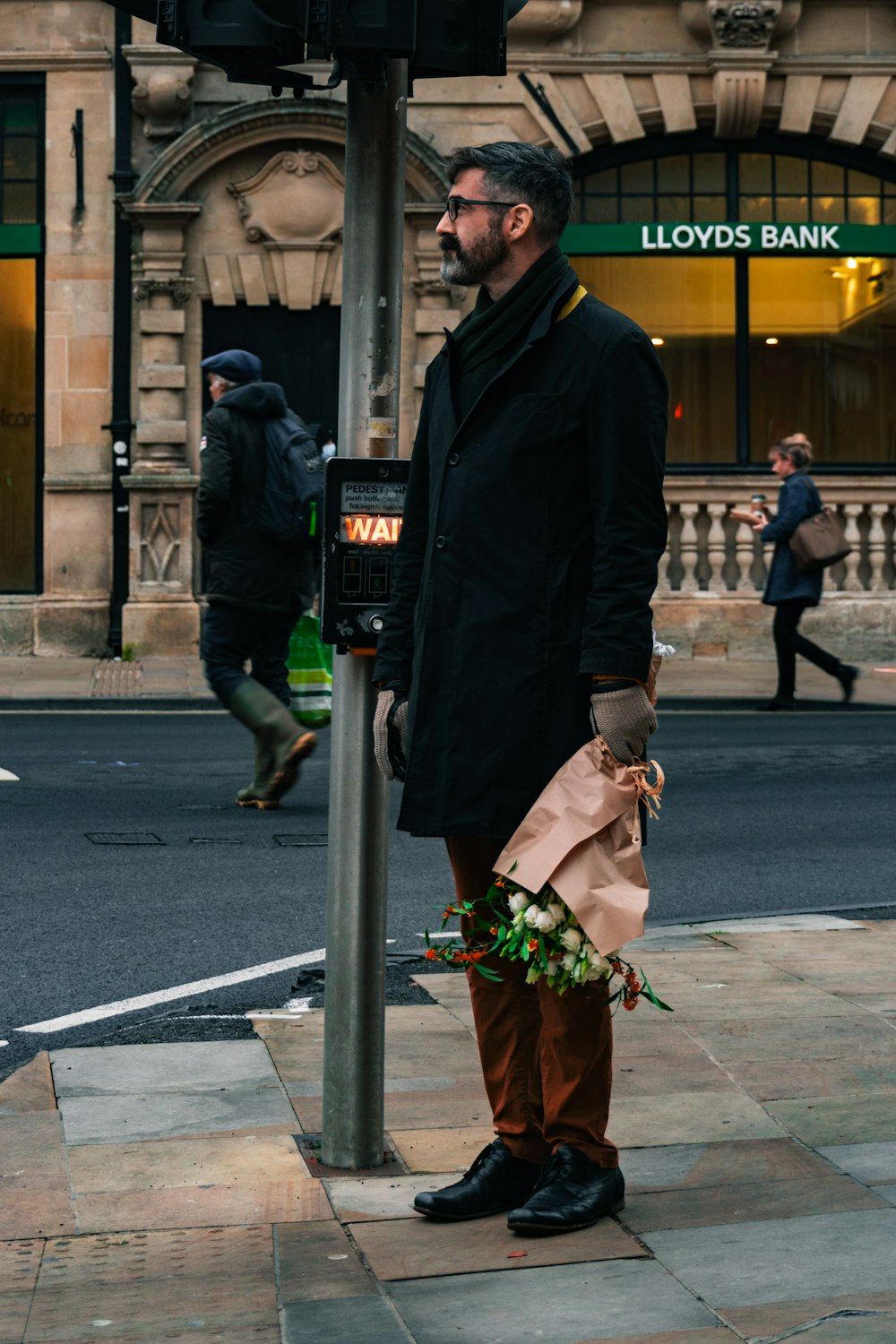 man in black coat holding green and red flower bouquet standing on sidewalk during daytime