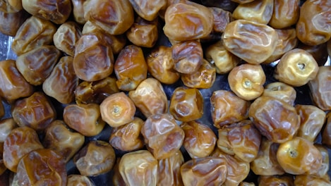 A close-up view of a large number of dried dates, showcasing their wrinkled texture and golden-brown color. The dates are heaped together, filling the entire frame.
