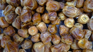 A close-up view of a large number of dried dates, showcasing their wrinkled texture and golden-brown color. The dates are heaped together, filling the entire frame.