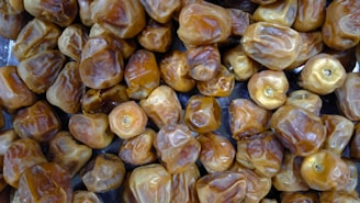 A close-up view of a large number of dried dates, showcasing their wrinkled texture and golden-brown color. The dates are heaped together, filling the entire frame.