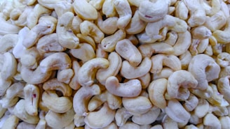 A pile of shelled cashew nuts with a creamy off-white color. The cashews are all similar in shape, with a curved, crescent-like appearance, and are densely packed together.