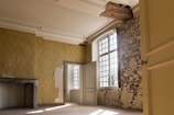 Worker carefully removing wallpaper in a bright residential room.