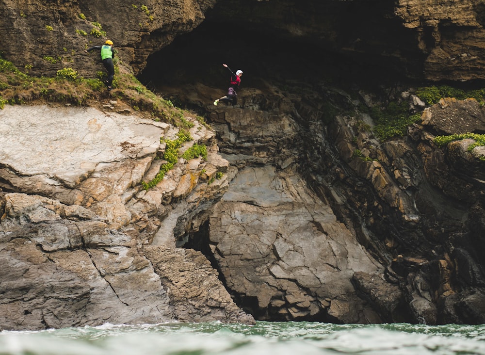 person in red shirt and black pants standing on rock formation near body of water during