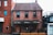 A red brick building with two stories features diamond-patterned windowpanes. The facade includes a dark awning with various brand names like Lamb's, J.P. Wiser's, and Absolut displayed. The structure has a small outdoor area with a black railing and a wooden door visible.
