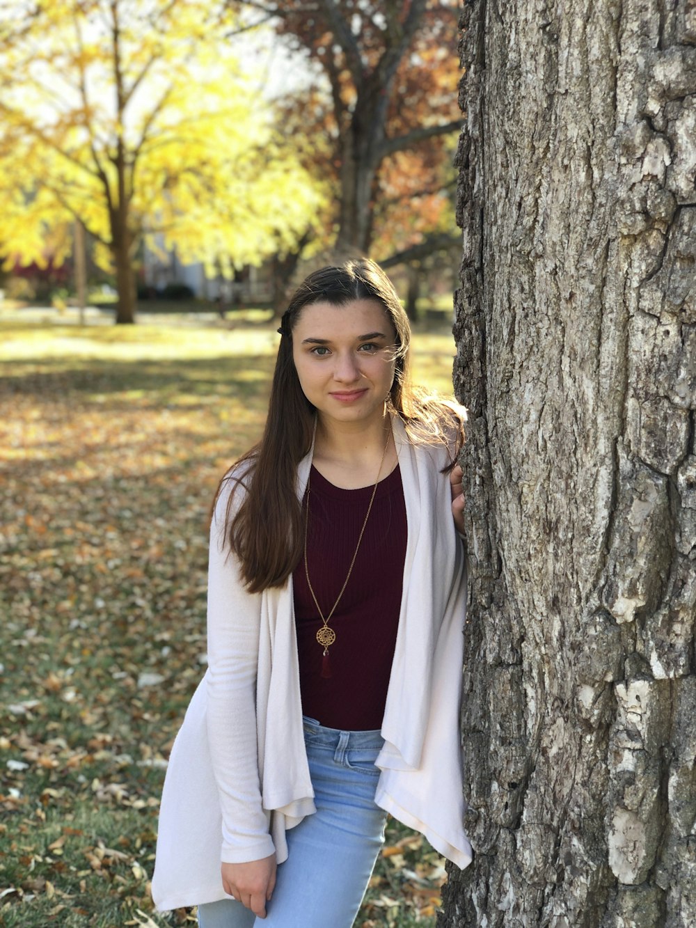 woman in white cardigan standing beside brown tree during daytime