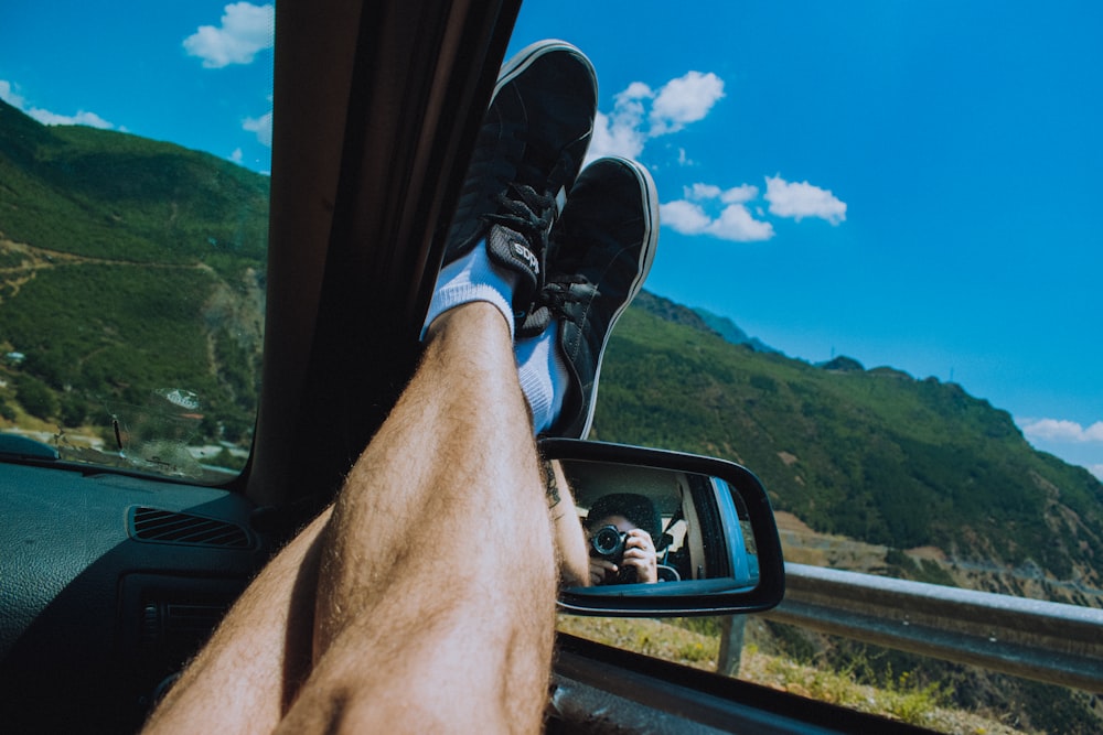 person in black and white nike sneakers sitting on car window during daytime