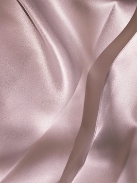 Soft, flowing fabric with a smooth, shiny texture featuring gentle folds and a subtle sheen, creating an elegant and luxurious appearance.