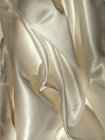 Smooth, shiny fabric with flowing, curved surfaces and soft folds in a light, creamy color.