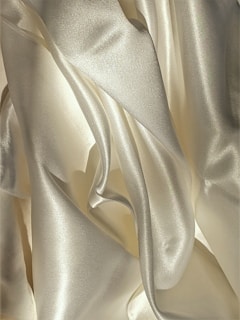 Smooth, shiny fabric with flowing, curved surfaces and soft folds in a light, creamy color.
