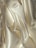 Smooth, shiny fabric with flowing, curved surfaces and soft folds in a light, creamy color.