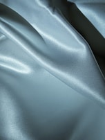 Smooth, shiny fabric with a silky texture featuring soft folds and a light reflection that adds depth and texture to the surface.