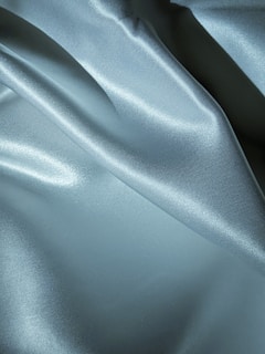 Smooth, shiny fabric with a silky texture featuring soft folds and a light reflection that adds depth and texture to the surface.