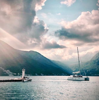 white sail boat on body of water near mountain under cloudy sky during daytime