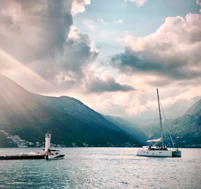 white sail boat on body of water near mountain under cloudy sky during daytime