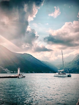 white sail boat on body of water near mountain under cloudy sky during daytime