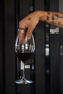 Close-up of a hand holding a glass of red wine next to a canvas with poetic calligraphy.