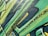 Graffiti art with bold, angular shapes and vibrant colors covers a textured wall. The design incorporates layers of green, yellow, and black with splashes of paint. The style suggests a dynamic and energetic feel, achieved through the use of sharp lines and contrasting shades.