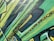 Graffiti art with bold, angular shapes and vibrant colors covers a textured wall. The design incorporates layers of green, yellow, and black with splashes of paint. The style suggests a dynamic and energetic feel, achieved through the use of sharp lines and contrasting shades.