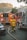 A firefighter in yellow protective gear with the initials LAFD is walking towards several fire trucks parked on a street. Thick fire hoses are spread across the road, and the background shows trees and a building under a hazy sky.