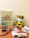 A teddy bear wearing a face mask is seated on a wooden surface beside a health guide chart depicting a food pyramid. Several medical items, including a stethoscope, blood pressure monitor, tablets, and an infrared thermometer, surround the teddy bear.