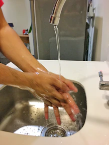Close-up of hands washing thoroughly under running water with soap in a bright kitchen.