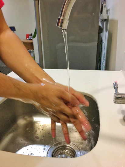 Close-up of hands washing thoroughly under running water with soap in a bright kitchen.