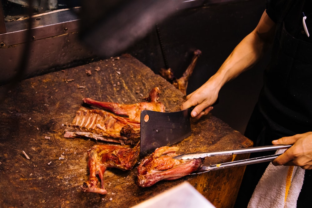 persona que sostiene cuchillo y tenedor cortando carne