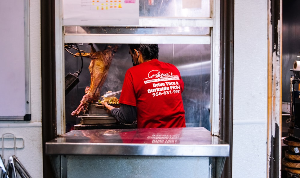 man in red hoodie sitting in front of cooked chicken