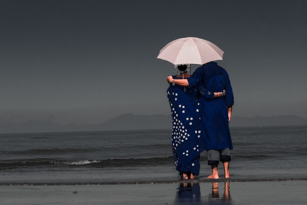 낮 동안 해변에서 우산을 들고 파란색과 흰색 꽃 드레스를 입은 여자