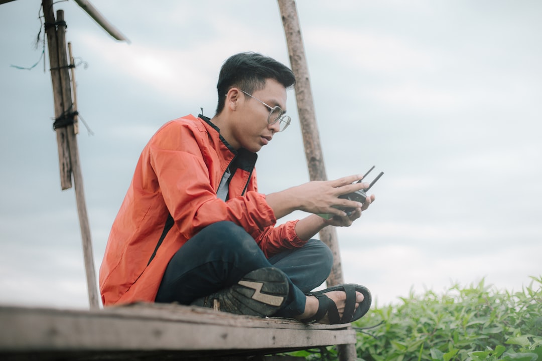 man in orange jacket sitting on brown wooden bench during daytime