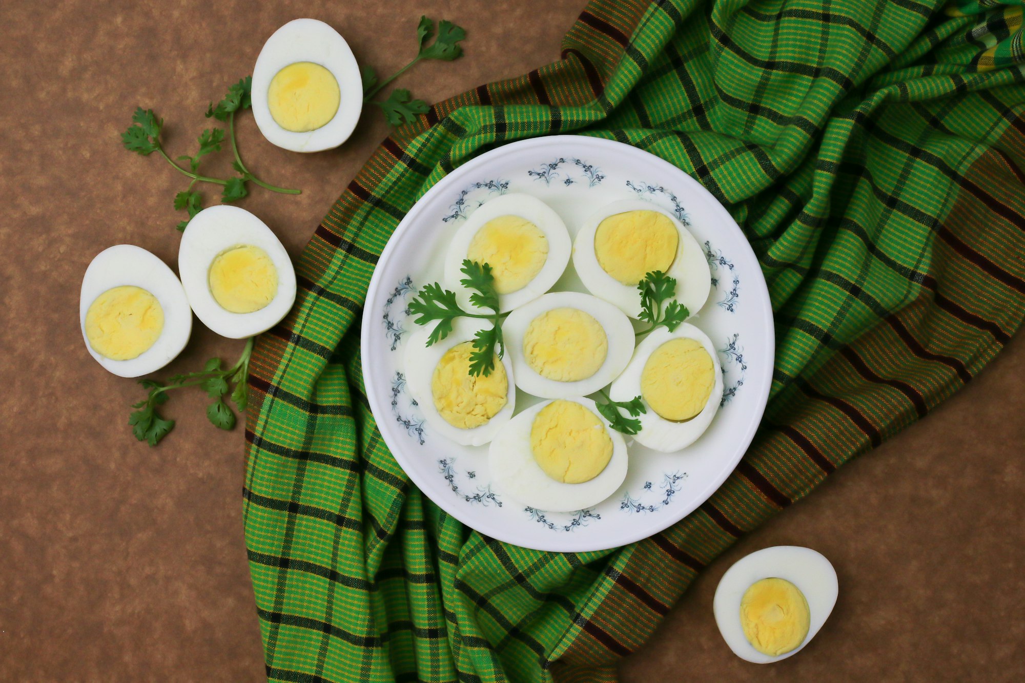 Sliced boiled eggs on white plate with green parsley leaves.

