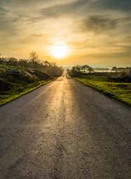 gray concrete road between green grass field under cloudy sky during daytime