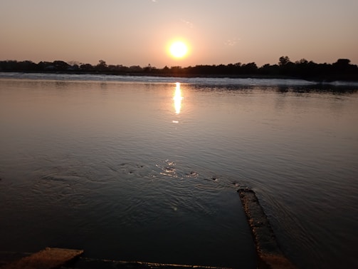 Sunset over the Arkansas River with silhouetted trees and a calm water reflection.