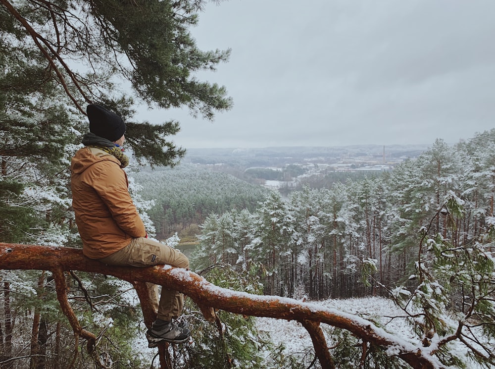 man in brown jacket sitting on tree branch during daytime