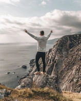 man in white dress shirt standing on brown rock formation near body of water during daytime