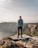man in blue jacket standing on rock formation near body of water during daytime