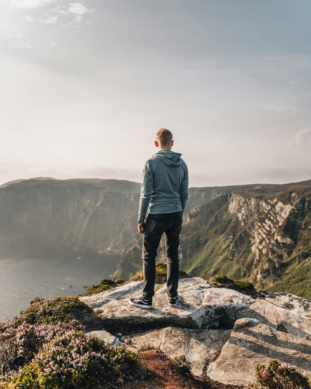 man in blue jacket standing on rock formation near body of water during daytime