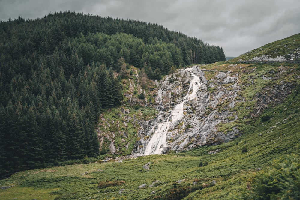 green grass field near waterfalls under cloudy sky during daytime