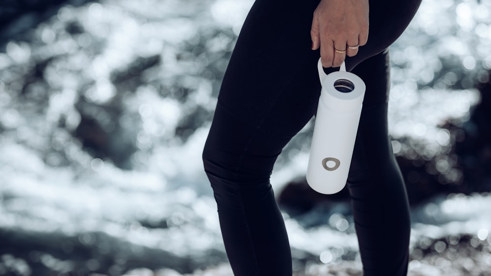 person in black pants holding white ceramic mug